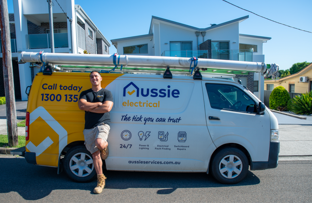 The electrician posing in front of their Aussie Electrical and Plumbing company van.